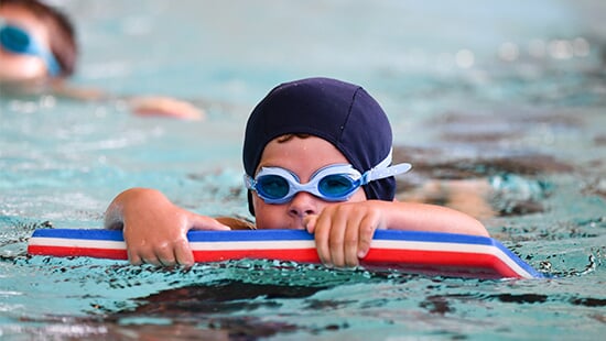 Un enfant nageant avec une planche lors d'une séance d'apprentissage de la nage